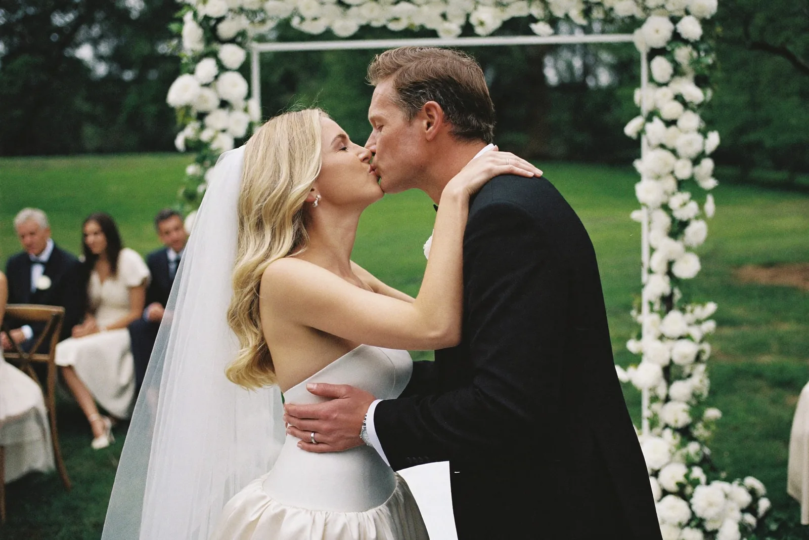 Outdoor garden wedding ceremony first kiss under a floral arch
