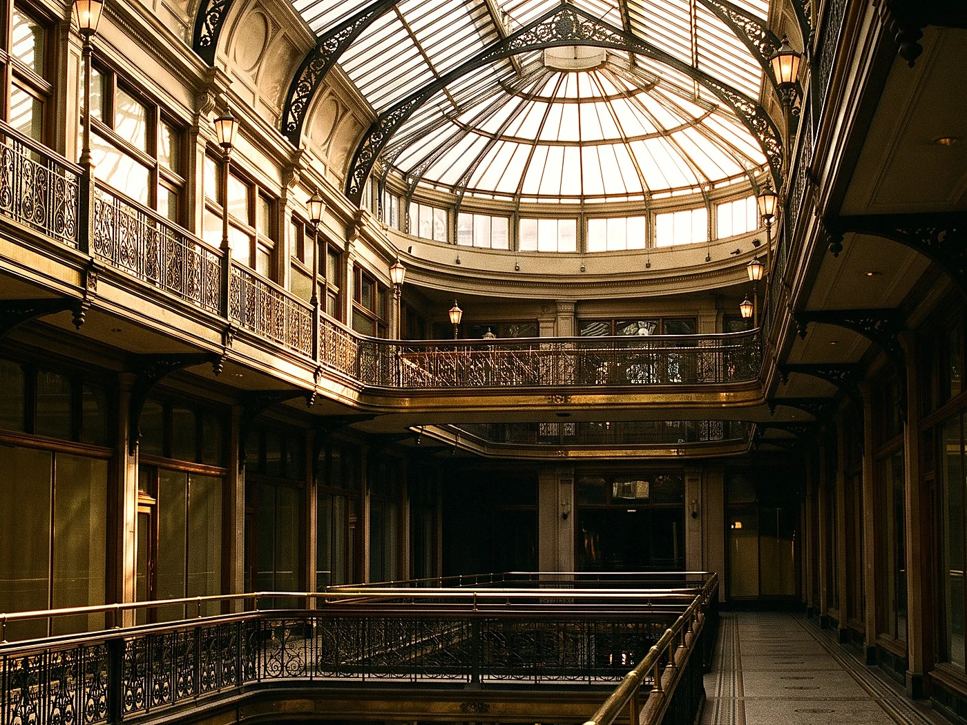 A grand Victorian arcade interior with glass skylight and brass railings glowing at golden hour.