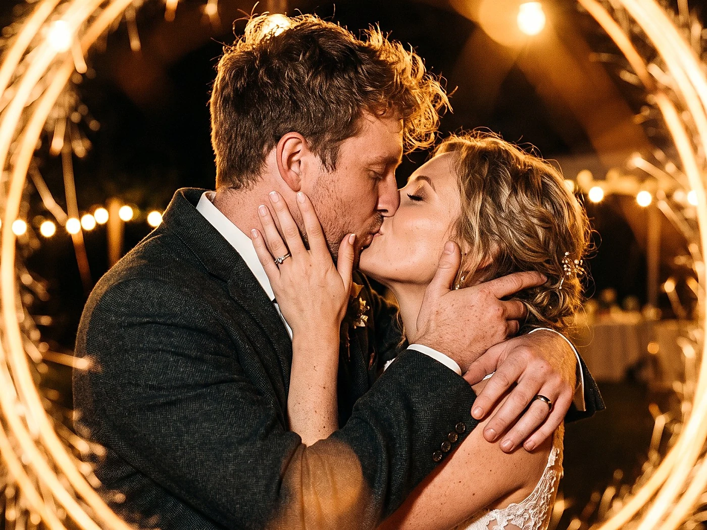 A couple kissing inside a warm ring of sparkler light at night, close crop.