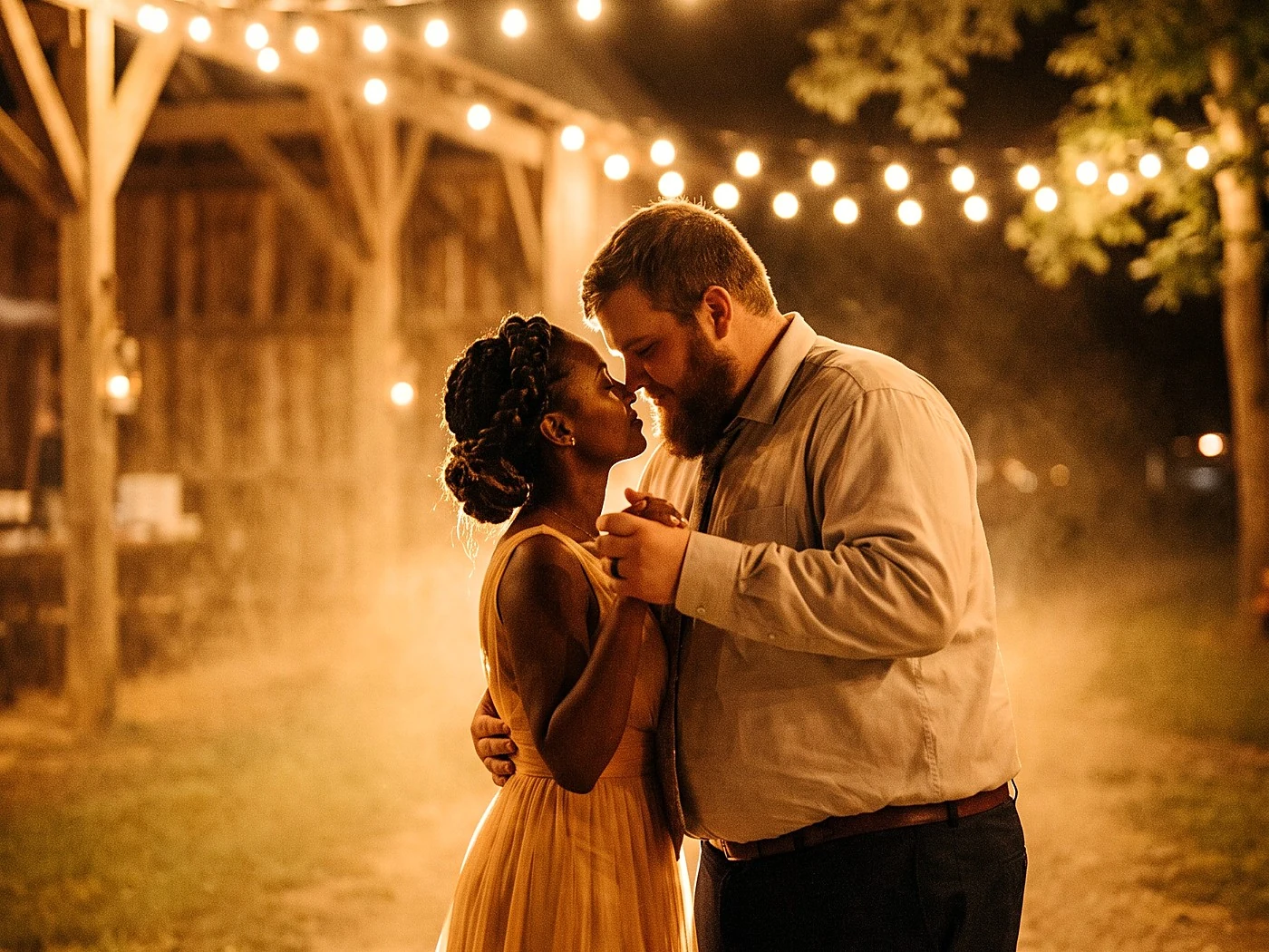 A couple slow dancing alone outside at night, barn string lights behind, her gown glowing amber.