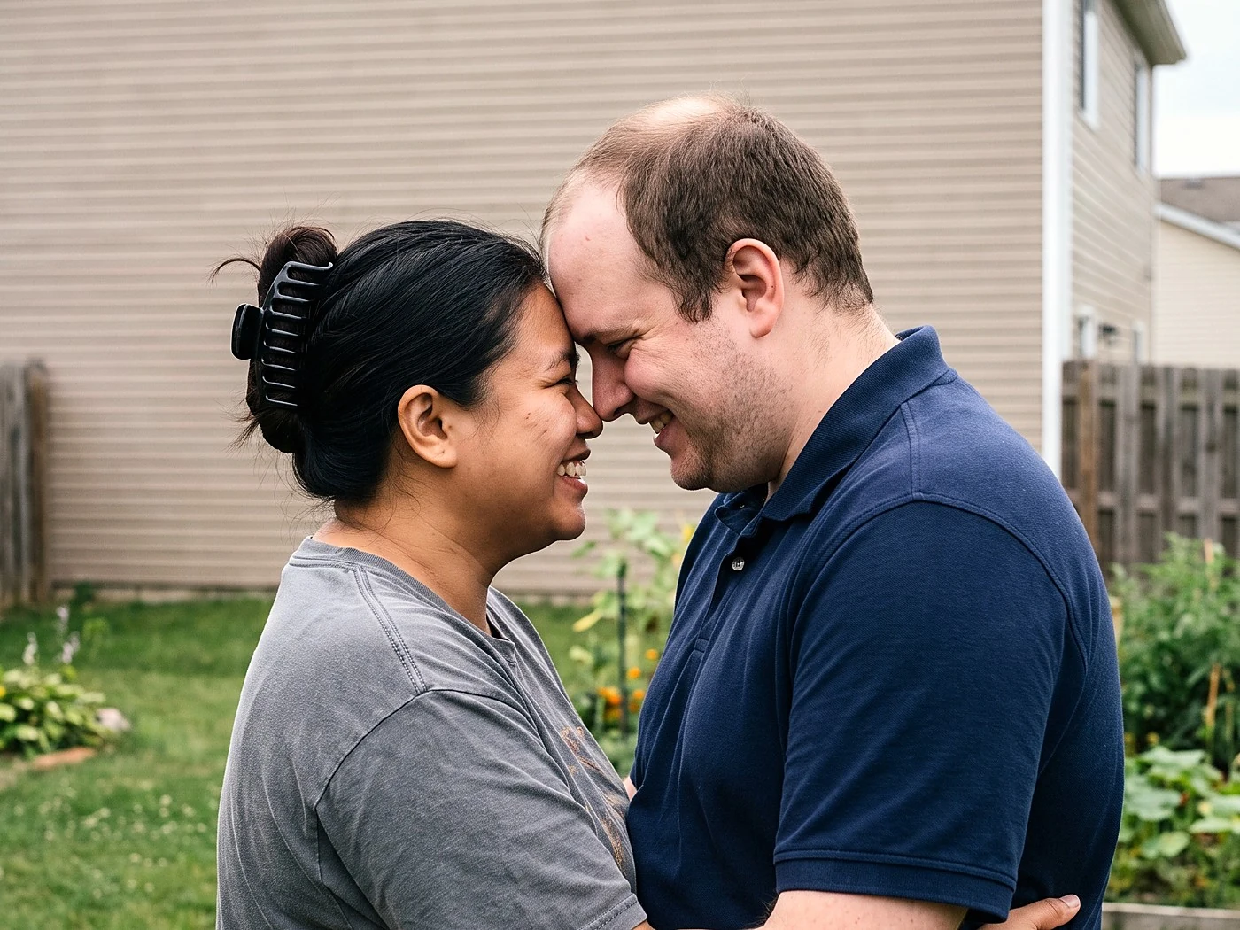 A regular couple embracing candidly in a backyard during their engagement session.