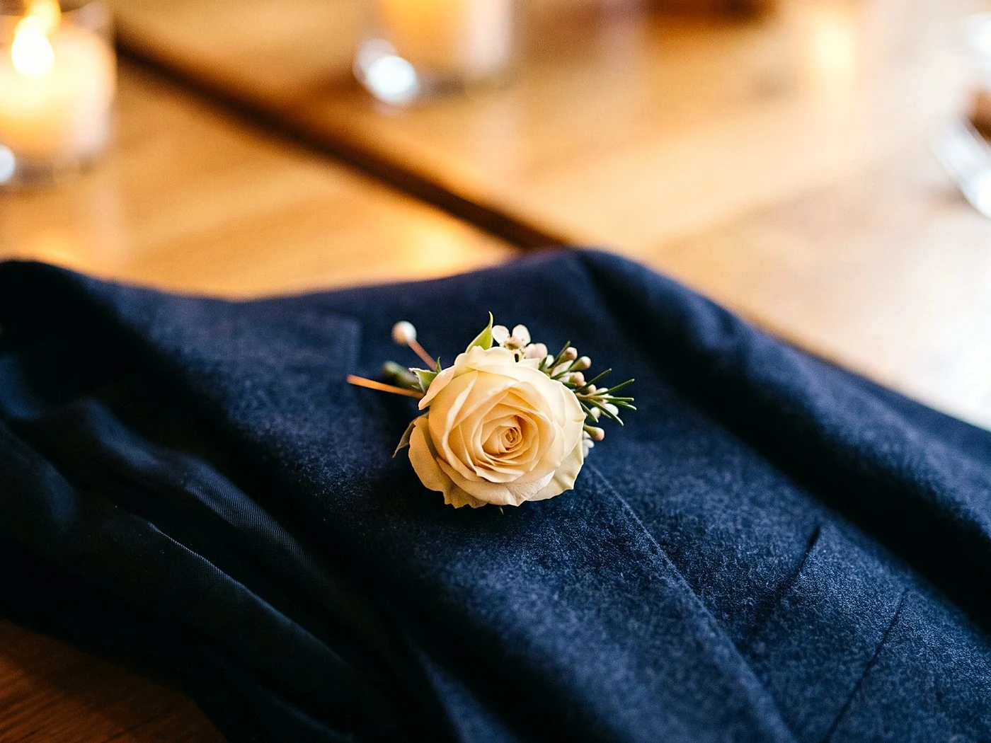 A single cream rose boutonniere lying on a folded navy lapel, macro detail.